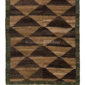 May include: A rectangular rug with a geometric pattern of brown and dark brown triangles. The rug has a green border and a cream-colored fringe. The text "Bespoke Handmade Rugs" is visible on the rug.