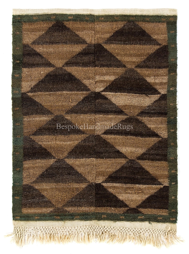May include: A rectangular rug with a geometric pattern of brown and dark brown triangles. The rug has a green border and a cream-colored fringe. The text "Bespoke Handmade Rugs" is visible on the rug.