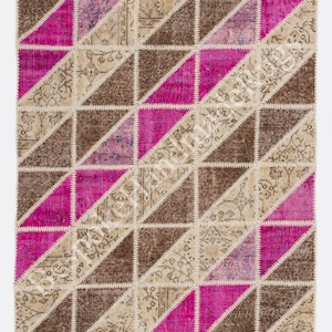 Könnte beinhalten: Ein rechteckiger Patchwork-Teppich mit einem sich wiederholenden geometrischen Muster aus Dreiecken in Braun-, Beige- und leuchtenden Magentatönen. Die einzelnen Stoffsegmente sind durch sichtbare weiße Zickzacknähte miteinander verbunden.