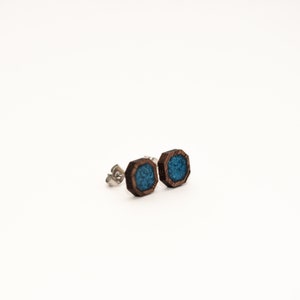 Peut inclure: Une paire de boucles d'oreilles en bois avec un design g&eacute;om&eacute;trique. Les boucles d'oreilles pr&eacute;sentent un cadre en bois brun fonc&eacute; avec un centre de couleur turquoise. Les tiges sont en m&eacute;tal argent&eacute;. Sur fond blanc.