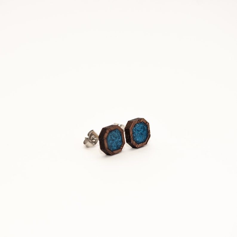 Peut inclure: Une paire de boucles d'oreilles en bois avec un design g&eacute;om&eacute;trique. Les boucles d'oreilles pr&eacute;sentent un cadre en bois brun fonc&eacute; avec un centre de couleur turquoise. Les tiges sont en m&eacute;tal argent&eacute;. Sur fond blanc.