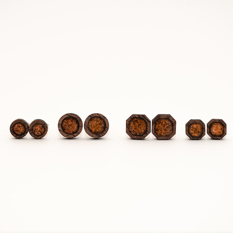 May include: Set of six wooden earrings with a brown wood finish and a brown and orange speckled center. The earrings are in three different shapes: round, octagon, and small round.