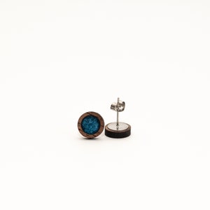 Peut inclure: Une paire de boucles d'oreilles rondes. Chaque boucle d'oreille pr&eacute;sente un cadre en bois fonc&eacute; avec un centre de couleur teal. Les tiges des boucles d'oreilles sont en m&eacute;tal argent&eacute;. Les boucles d'oreilles sont pr&eacute;sent&eacute;es sur fond blanc.