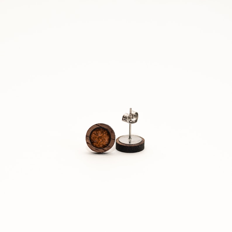May include: A pair of round wooden earrings with a brown wood frame and a brown and orange center. The earrings have silver posts.