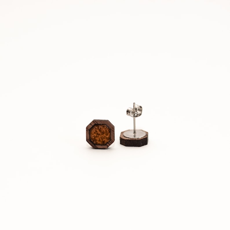 May include: A pair of wooden earrings with a brown octagonal shape and a brown and orange speckled center. The earrings have silver posts.