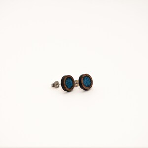 Peut inclure: Deux boucles d'oreilles rondes en bois, avec un cadre marron fonc&eacute; et un centre bleu turquoise. Les boucles d'oreilles ont un design simple et minimaliste, sur fond blanc. Les tiges sont argent&eacute;es.