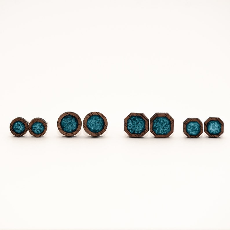 Peut inclure: Plusieurs boucles d'oreilles en bois avec un centre en r&eacute;sine turquoise. Les boucles d'oreilles sont de diff&eacute;rentes tailles et formes, notamment rondes et octogonales. Le bois est de couleur marron fonc&eacute; et la r&eacute;sine a un aspect marbr&eacute;.