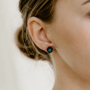 Peut inclure: Gros plan sur une boucle d'oreille en bois avec un motif g&eacute;om&eacute;trique. La boucle d'oreille a un cadre en bois brun fonc&eacute; avec un centre de couleur turquoise. La boucle d'oreille est sur l'oreille d'une personne.