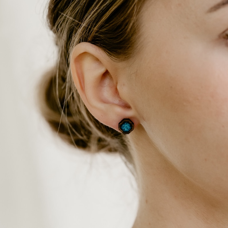 Peut inclure: Gros plan sur une boucle d'oreille en bois avec un motif g&eacute;om&eacute;trique. La boucle d'oreille a un cadre en bois brun fonc&eacute; avec un centre de couleur turquoise. La boucle d'oreille est sur l'oreille d'une personne.