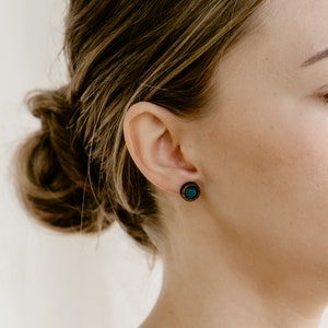 Peut inclure: Gros plan sur une oreille orn&eacute;e d'une boucle d'oreille en bois. La boucle d'oreille a un bord en bois fonc&eacute; et un centre turquoise. Les cheveux de la personne sont attach&eacute;s en chignon.