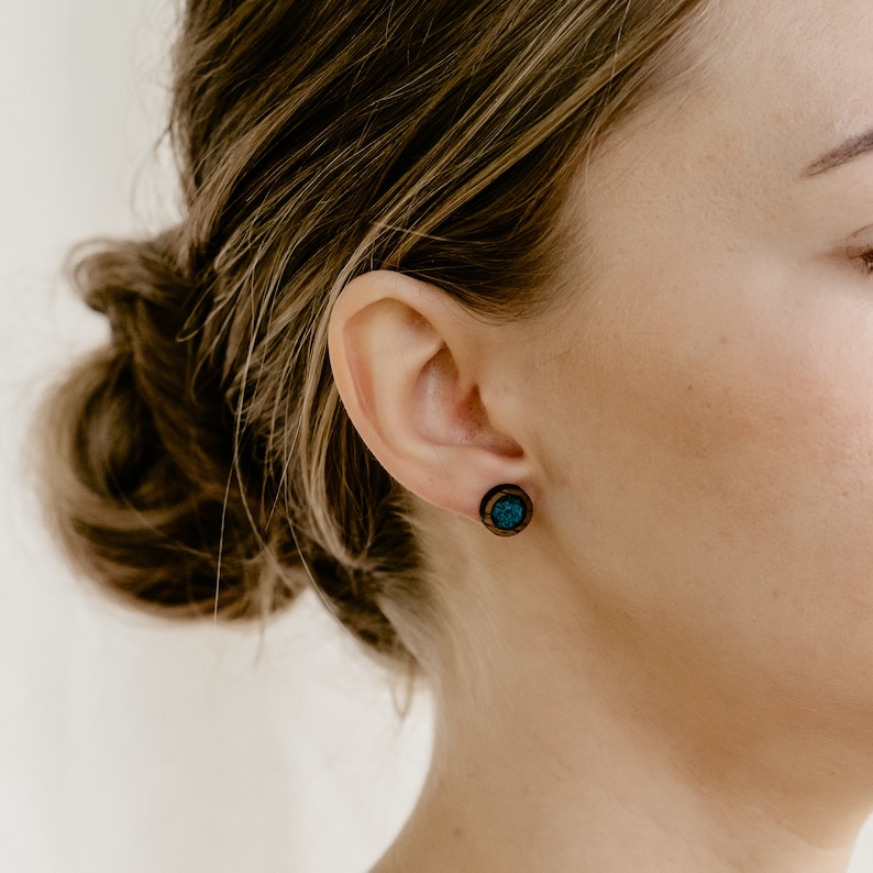 Peut inclure: Gros plan sur une oreille orn&eacute;e d'une boucle d'oreille en bois. La boucle d'oreille a un bord en bois fonc&eacute; et un centre turquoise. Les cheveux de la personne sont attach&eacute;s en chignon.