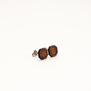 May include: A pair of brown wooden earrings with a hexagonal shape. The earrings have a silver post and back.