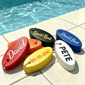 Pode incluir: Um conjunto de seis porta-chaves de espuma de formato oval nas cores vermelha, laranja, preta, amarela, azul e branca. Cada porta-chaves possui uma corrente de metal e texto personalizado, incluindo David, David's Boat, 914-141-3242 e PETE.