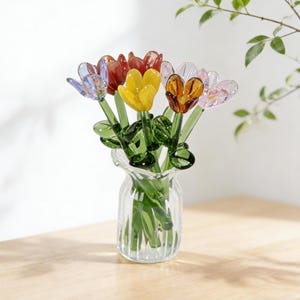 Peut inclure: Un petit vase en verre rempli de tulipes en verre colorées. Les tulipes sont de couleurs bleu, rouge, jaune et orange. Les tiges et les feuilles sont vertes. Le vase transparent a un design côtelé.