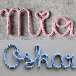 Op de afbeelding: Twee namen, Mia en Oskar, gespeld in garen. Mia is in roze garen en Oskar is in blauw garen.