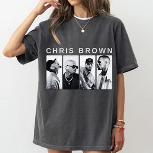 Pu&ograve; includere: T-shirt grigio scuro con la scritta "CHRIS BROWN" sopra quattro immagini in bianco e nero dell'artista. La maglietta ha maniche corte e girocollo.