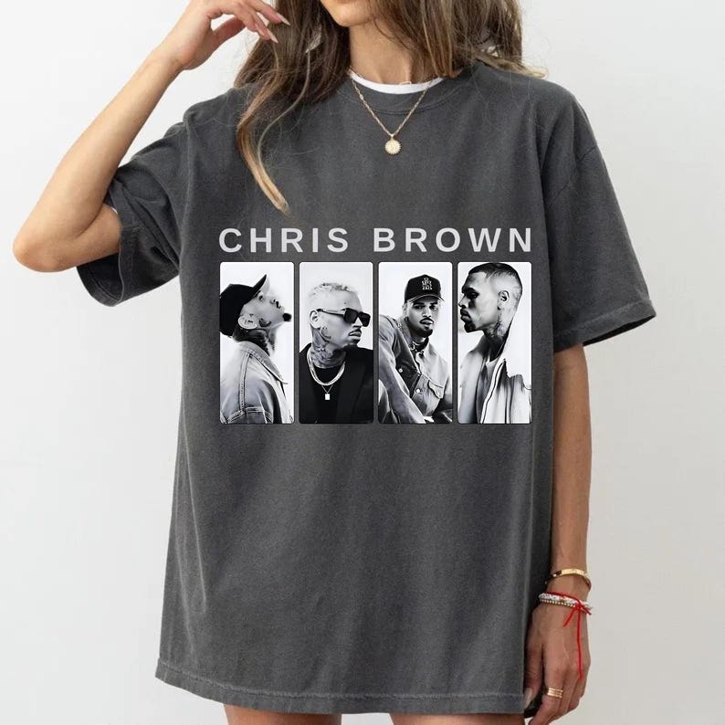 Pu&ograve; includere: T-shirt grigio scuro con la scritta "CHRIS BROWN" sopra quattro immagini in bianco e nero dell'artista. La maglietta ha maniche corte e girocollo.