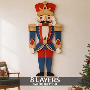 May include: A wall-mounted wooden nutcracker decoration featuring 8 layers of cut wood. The figure is painted in red, blue, gold, and white, with a black mustache, a tall hat, and epaulets. The text 8 LAYERS SVG CDR DXF PDF AI is visible.
