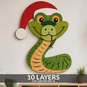 Puede incluir: Una pieza de arte mural de madera multicapa con forma de serpiente verde que lleva un gorro de Papá Noel rojo y blanco. La serpiente tiene grandes ojos amarillos, una cara sonriente y una lengua roja. El cuerpo presenta un vientre amarillo.