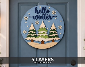 May include: A circular wooden door sign featuring a light blue background with the dark blue text hello winter. The design includes three layered pine trees with green and white snow-capped branches, brown trunks, and several white snowflakes.