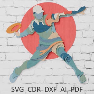 May include: A layered wooden art piece depicting a person throwing a frisbee, set against a red circle and a white brick wall. The figure is in shades of blue, green, and tan, holding an orange frisbee. The text "SVG CDR DXF AI PDF" is at the bottom.