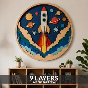 May include: A circular multi-layered wooden wall art piece featuring a central rocket ship launching into space. The design includes layered clouds in shades of blue and tan, planets with rings, and stars against a dark blue background.