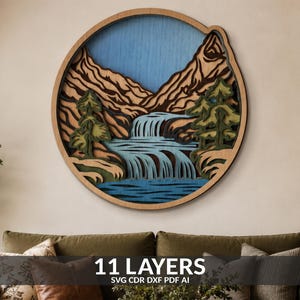 Pode incluir: Uma arte de parede circular de madeira com várias camadas, apresentando uma paisagem montanhosa com uma cascata, árvores perenes e um céu azul. O design é composto por 11 camadas distintas de madeira em tons naturais e tinta azul.