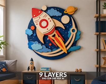 May include: A circular wooden wall art piece featuring a multi-layered rocket ship design in red, orange, and natural wood tones. The rocket is set against a dark blue circular background with blue clouds, planets, and stars. Text reads 9 LAYERS.