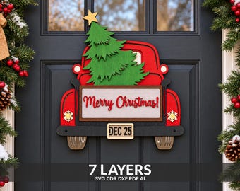 May include: A layered wooden door sign shaped like a red truck carrying a green Christmas tree. The truck features a white sign with the red text Merry Christmas, a license plate reading DEC 25, and gold snowflake accents on the rear fenders.