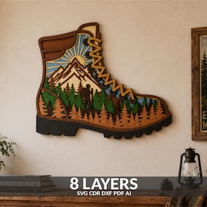 May include: A multi-layered wooden wall art piece shaped like a hiking boot. The design features a mountain landscape with a sun, a forest of pine trees, and a hiker silhouette. The layers are stained in shades of brown, green, and blue.