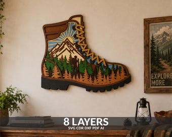 May include: A multi-layered wooden wall art piece shaped like a hiking boot. The design features a mountain landscape with a sun, a forest of pine trees, and a hiker silhouette. The layers are stained in shades of brown, green, and blue.