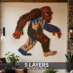 May include: A multi-layered wooden wall art piece shaped like a Bigfoot silhouette. The design features five distinct layers with cutouts of pine trees and forest landscapes in shades of dark brown, light brown, blue, and green. Text reads 5 LAYERS SVG CDR DXF PDF AI.