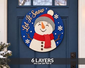 May include: A circular wooden door sign featuring a smiling snowman with a red hat, a red scarf, and an orange carrot nose. The blue background displays the text Let It Snow in script lettering, accented by white snowflakes and small dots.