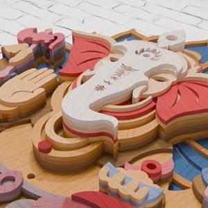 May include: A multi-layered wooden wall art piece depicting the deity Ganesha. The design features stacked laser-cut wood panels in shades of natural wood, red, and blue, forming the elephant head, lotus petals, and symbolic hand gestures.