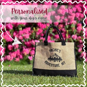 May include: A beige burlap tote bag with black trim and handles, set on grass against a backdrop of pink flowers. The bag is printed with "Archie's Adventure Kit" and is designed to be personalised with a dog's name.