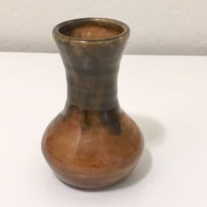 May include: A small ceramic vase with a bulbous base and a flared neck. The piece features a glossy glaze with a gradient of warm amber and orange tones at the bottom, transitioning into a darker, muted brown finish toward the top rim.