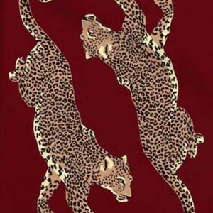 Könnte beinhalten: Zwei stilisierte Leopardenfiguren mit schwarzen Flecken und hellbraunen Markierungen vor einem tiefroten Hintergrund. Die Leoparden befinden sich in dynamischen Posen, einer reckt sich nach oben, der andere geht. Das Design weckt ein Gefühl von Bewegung und Wildheit.
