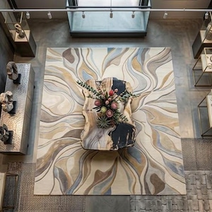 May include: An interior design display featuring a large, abstract rug with swirling patterns in beige, brown, and blue tones. A wooden sculpture with floral arrangements is mounted on the rug. Display cases with jewellery and artwork are visible.