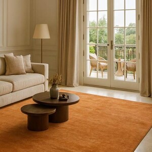 Puede incluir: Una sala de estar con una gran alfombra de color &oacute;xido. Dos mesas de centro redondas de color marr&oacute;n oscuro est&aacute;n sobre la alfombra. Un sof&aacute; beige y una l&aacute;mpara de pie tambi&eacute;n son visibles. Las puertas francesas dan a un balc&oacute;n.