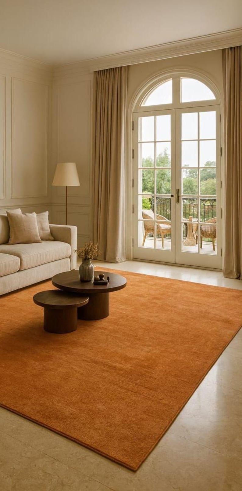 Puede incluir: Una sala de estar con una gran alfombra de color &oacute;xido. Dos mesas de centro redondas de color marr&oacute;n oscuro est&aacute;n sobre la alfombra. Un sof&aacute; beige y una l&aacute;mpara de pie tambi&eacute;n son visibles. Las puertas francesas dan a un balc&oacute;n.
