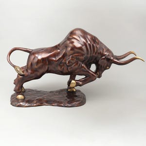 Può includere: Scultura in bronzo di un toro in carica con patina marrone scuro. Il toro presenta dettagli dorati su zoccoli e corna. La scultura, su una base strutturata, rappresenta forza e potenza.