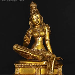 May include: A golden statue of a seated female figure, adorned with intricate jewelry and a tall headdress. The figure is seated on a detailed pedestal. The statue is made of a shiny, reflective metal, and the overall aesthetic is one of elegance and cultural significance.