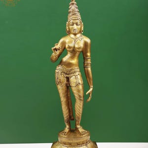May include: A golden-colored statue of a standing figure with intricate details. The figure wears a tall, ornate headdress and detailed clothing. The statue is mounted on a decorative base, set against a green background.