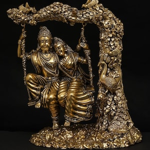 Puede incluir: Una escultura dorada de una pareja en un columpio, sobre un fondo oscuro. La escultura presenta detalles intrincados, incluyendo la ropa de las figuras y la estructura arbórea que sostiene el columpio. La base es texturizada y la escultura tiene una estética tradicional.