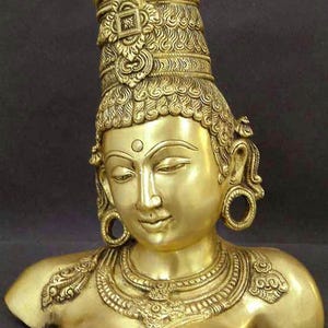 May include: A golden-colored bust of a deity with an ornate headdress and jewelry. The sculpture features detailed carvings, including a dot on the forehead and large hoop earrings. The figure has a serene expression.