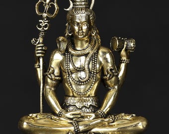 May include: A gold-colored statue of a seated deity, holding a trident and a small drum. The figure is adorned with intricate jewelry and a cobra around the neck. The base features a tiger-like face. The statue is against a dark background.