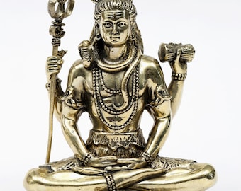 May include: A brass statue of a seated deity, holding a trident and a log. The figure is adorned with necklaces and a serpent, and sits atop a base with a tiger's head. The statue is from Exotic India.