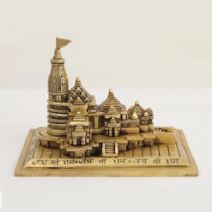 May include: A detailed brass sculpture of a temple with multiple domes, towers, and a flag. The base features engraved text. The sculpture is a golden colour and sits on a white background. The logo "exotic india" is in the top left corner.