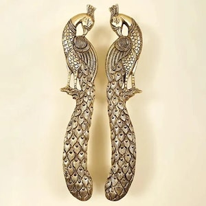 Pode incluir: Duas maçanetas ornamentadas em forma de pavão dourado. Cada maçaneta apresenta um design detalhado de pavão com coroa, intrincados padrões de penas e uma cauda curva. As maçanetas são simétricas e se destacam em um fundo neutro.