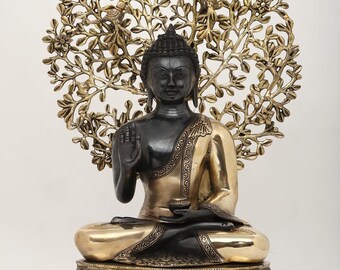 May include: A seated Buddha statue with a black head and upper body, and a gold-colored lower body and base. The statue is set against a gold-colored, circular, leafy backdrop with birds. The Buddha is in a meditative pose.